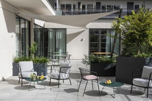 Ein moderner Außenbereich mit Tischen und Stühlen, umgeben von Kübelpflanzen und einem großen Fenster.