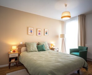 A bedroom with a bed, bedside tables, a floor lamp, a chair, and wall art. - Zenao Appart'hôtels Clichy (Clichy)