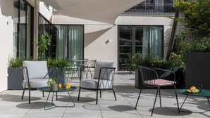 Un área de estar al aire libre con sillas y mesas modernas, y plantas en macetas.