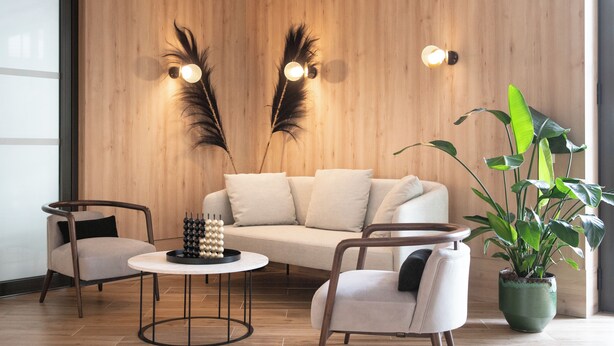 Una sala de estar moderna con un sofá, dos sillones, una mesa de centro, plantas decorativas e iluminación en la pared.