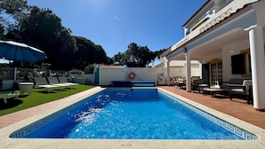 A swimming pool with a tiled edge, surrounded by a patio area with chairs and a table. - Vilamoura Summer Villa 3 by Homing (Loulé)