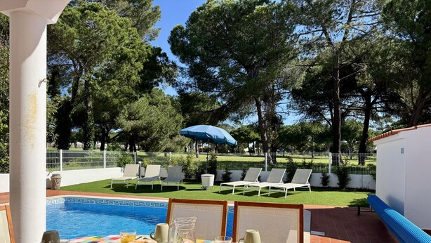 A poolside breakfast table with a view of the pool and trees. - Vilamoura Summer Villa 3 by Homing (Loulé)