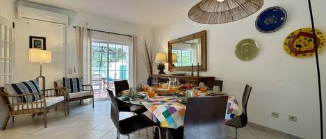 Un coin repas avec une table dressée pour quatre personnes, des chaises, une lampe et un miroir au mur.