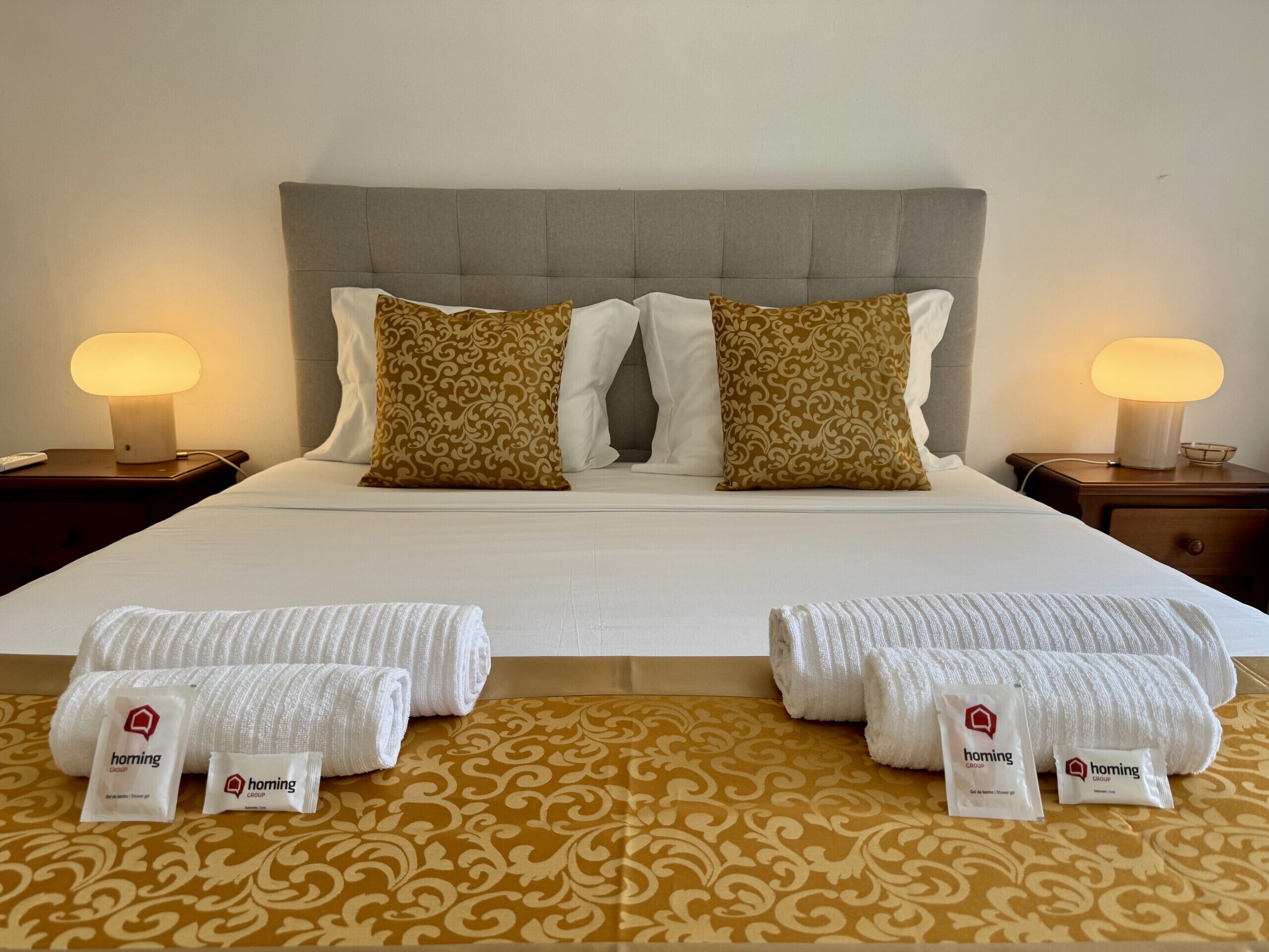 A hotel room with a bed, two nightstands, two lamps, and towels on the bed.