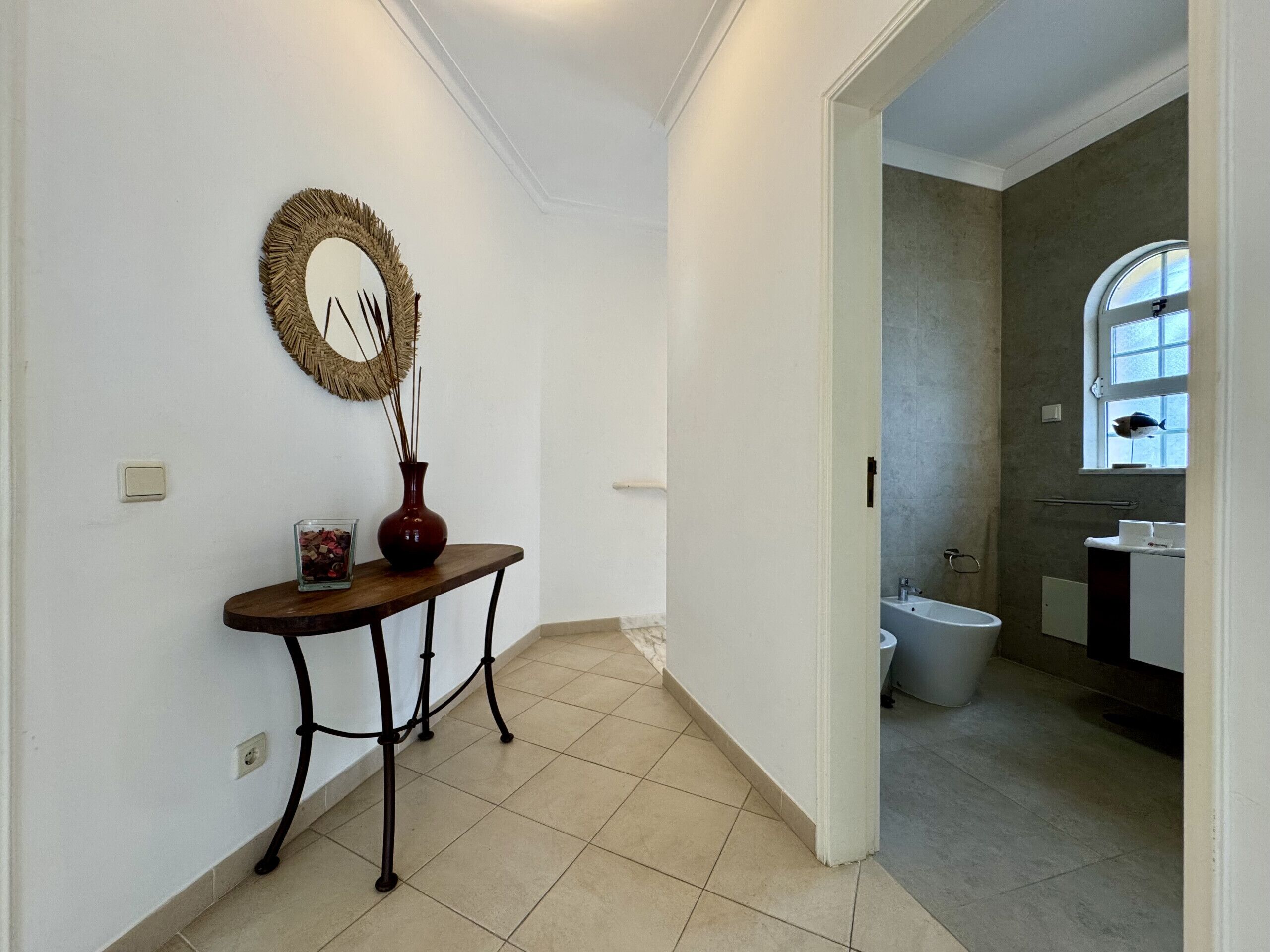 A hallway leading to a bathroom with a toilet, sink, and a window with a view.
