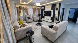 A modern living room with a sofa set, a coffee table, a TV, and a fireplace. - Liz Ani Apartment (Abuja)
