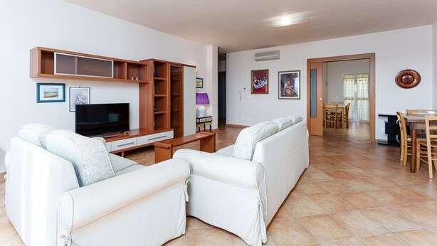 A living room with a TV, sofa, wooden cabinet, and dining area with chairs and a table. - Gandelli Holiday Home with Private Terrace, Wi-Fi and Air Conditioning (Orosei)