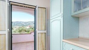 An open sliding door leading to a balcony with a view of distant mountains and a building. - Gandelli Holiday Home with Private Terrace, Wi-Fi and Air Conditioning (Orosei)