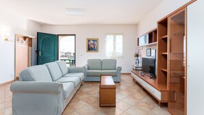 A living room with a sofa, a small table, a TV, and a wardrobe. - Gandelli Holiday Home with Private Terrace, Wi-Fi and Air Conditioning (Orosei)