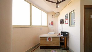 Una habitación pequeña con escritorio, una silla, ventilador de techo, extintor y ventana.