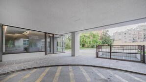 Een modern gebouw met grote glasramen, een verharde entree en uitzicht op omliggende gebouwen.