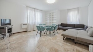 Een moderne woonkamer met een bank, een televisie, een eettafel met stoelen en een witte airconditioner.