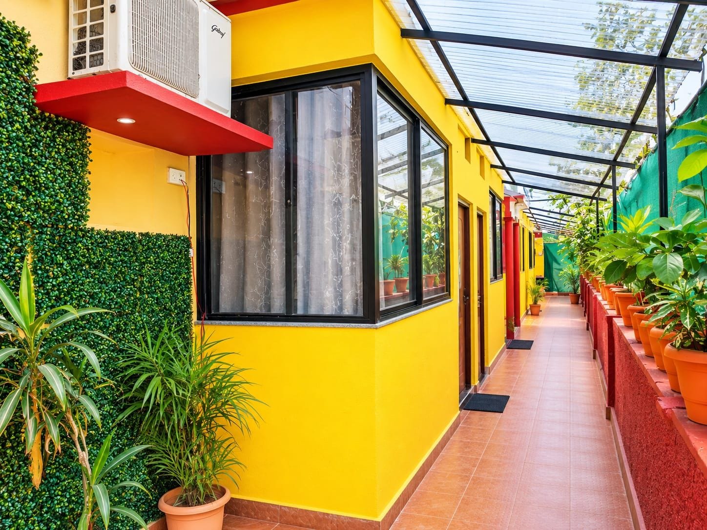 Un pasillo con plantas en macetas, una pared amarilla y una estructura de techo de cristal.