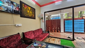 A room with a red sofa, a painting, a TV screen, and a view of a blue gate. - Poonam Grand (Calangute)