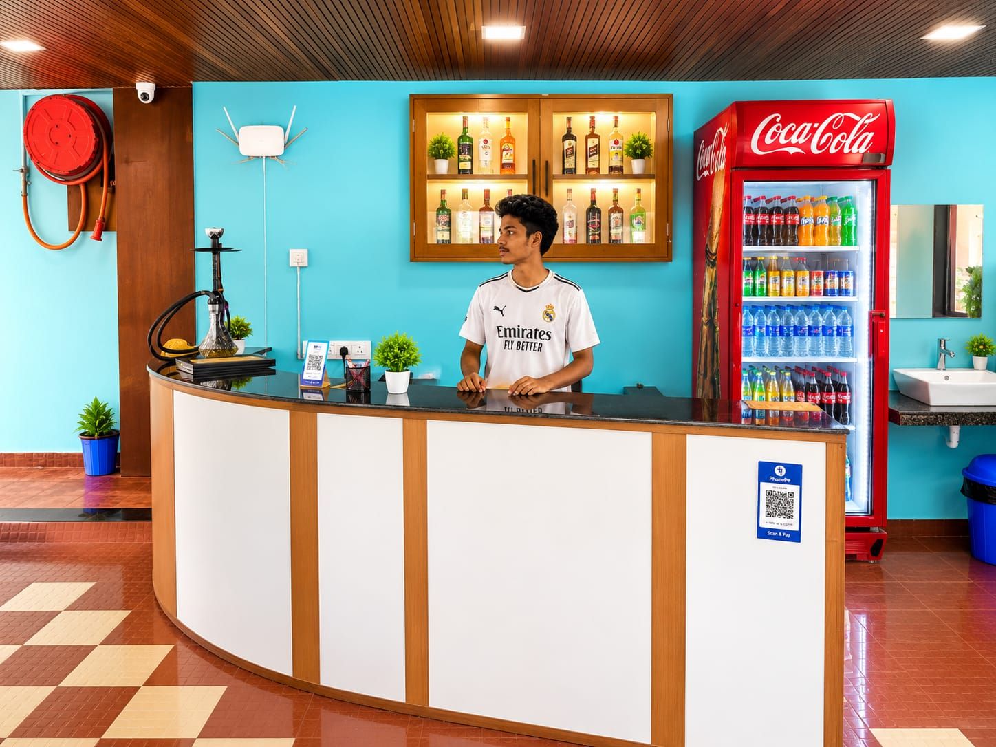 Zona de recepción de un hotel con mostrador, refrigerador de Coca-Cola y cámara de seguridad.