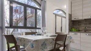 Un coin repas avec une table dressée pour quatre personnes, une fenêtre donnant sur un paysage arboré et une cuisine dotée de meubles modernes.