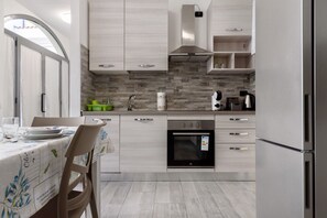 Una cocina moderna con armarios de madera clara, horno empotrado y refrigerador de acero inoxidable.