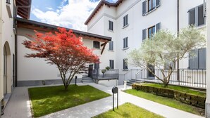 Une cour avec un bâtiment blanc, un chemin pavé et deux arbres aux feuilles rouges et blanches.