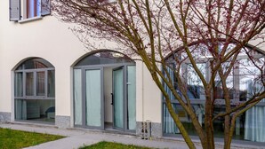 Un bâtiment doté de fenêtres en arc de cercle et d’une porte en verre, entouré d’une zone herbeuse avec un arbre.