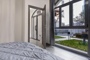 Une chambre avec un grand lit, une porte-fenêtre coulissante donnant sur un balcon et une vue sur l’extérieur.