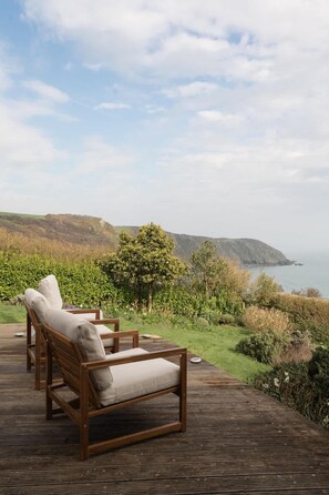 Una terraza de madera con dos sillones de descanso frente a un paisaje costero.