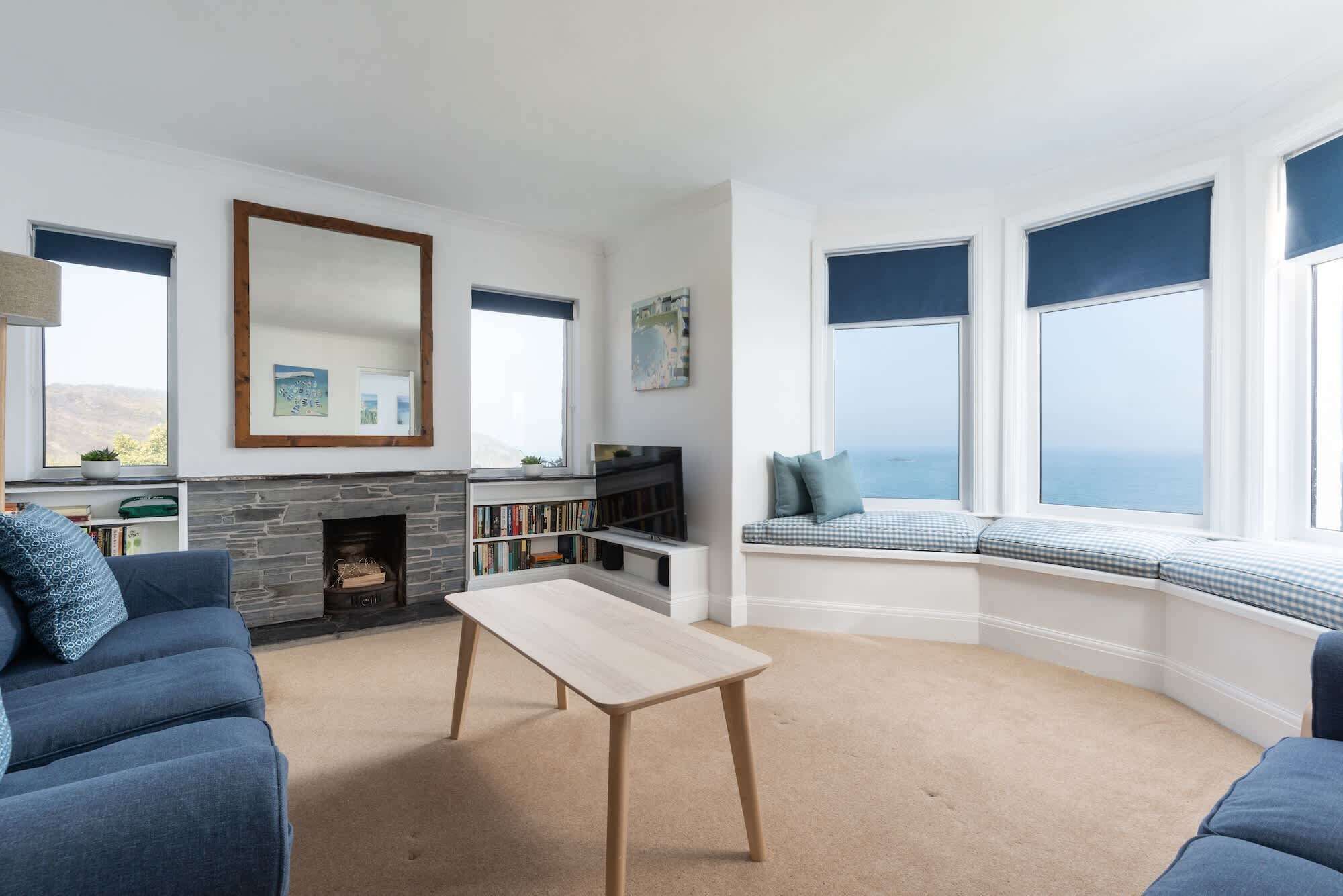 A living room with a fireplace, a bookshelf, a sofa, a coffee table, and a bay window with a view.