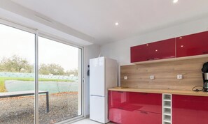 Une cuisine moderne dotée d’une porte-fenêtre coulissante, d’un réfrigérateur blanc, de meubles de rangement rouges et d’un plan de travail en bois.