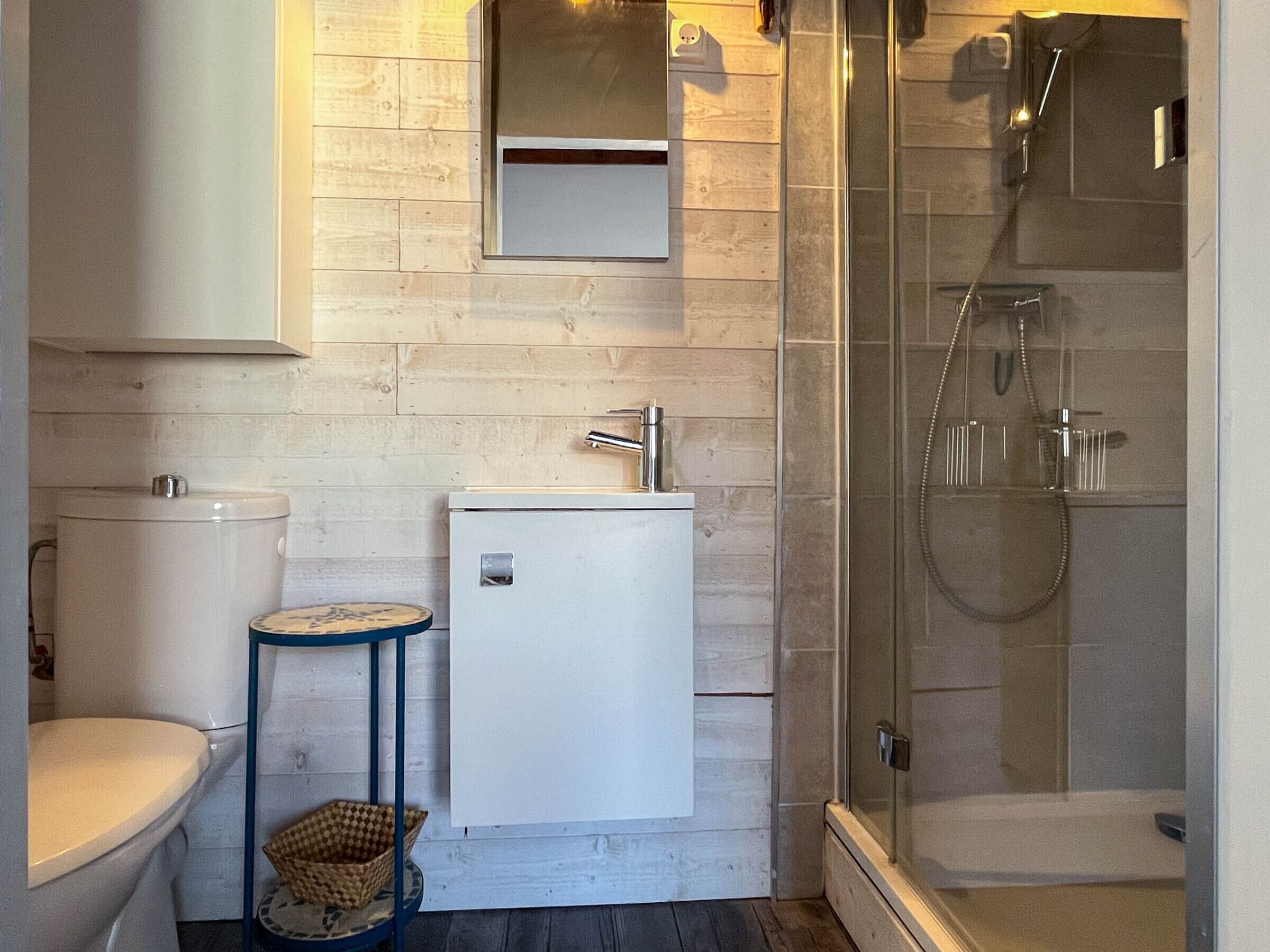 A compact bathroom with a toilet, a small sink, a mirror, and a glass-enclosed shower.