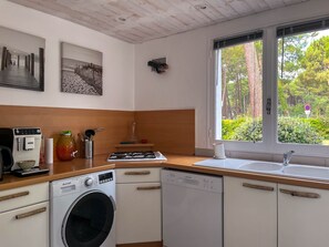 Une cuisine compacte équipée d’un lave-linge, d’une machine à café et d’une fenêtre donnant sur un espace verdoyant.
