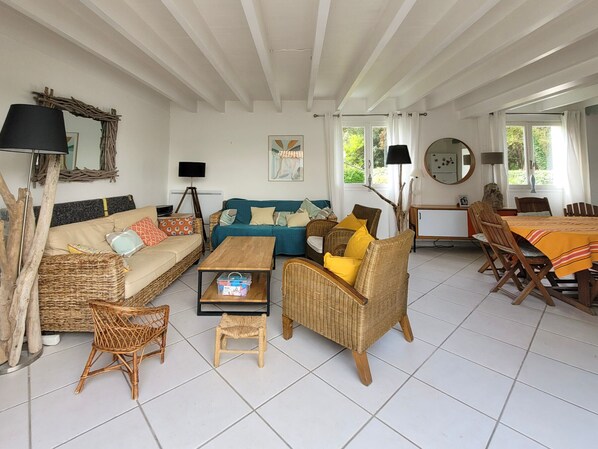 Ein Wohnzimmer mit Sofa, Sesseln, einem Couchtisch, einem Esstisch mit Stühlen und einem Fernseher.