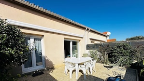Eine Terrasse mit Tisch und Stühlen, ein Grill und ein Haus mit einem Ziegeldach.