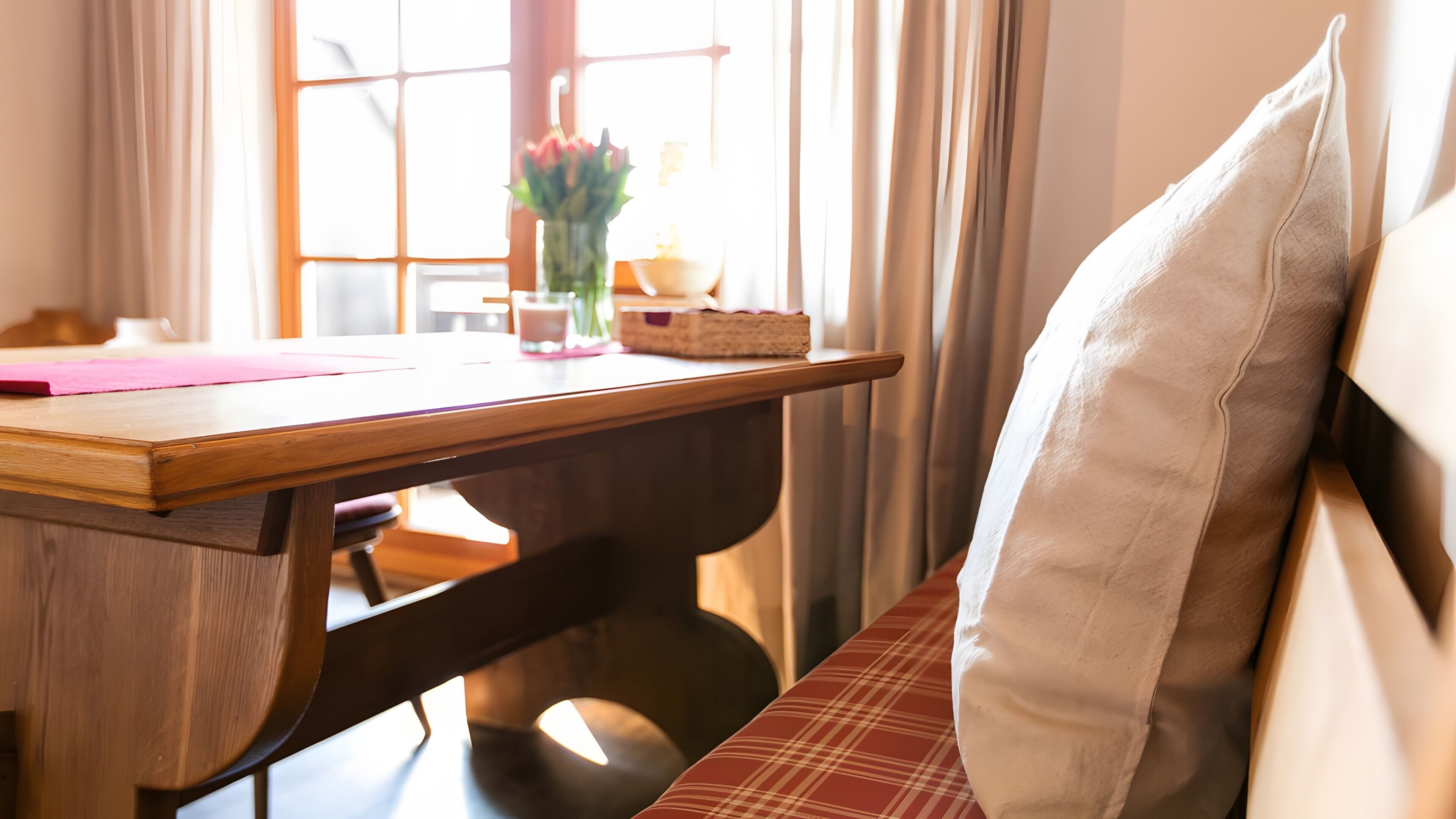A wooden table with a pink mat, a vase with flowers, and a candle on it.