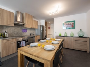 A modern kitchen with wooden cabinets, a granite countertop, and a dining area with a wooden table set for four.
