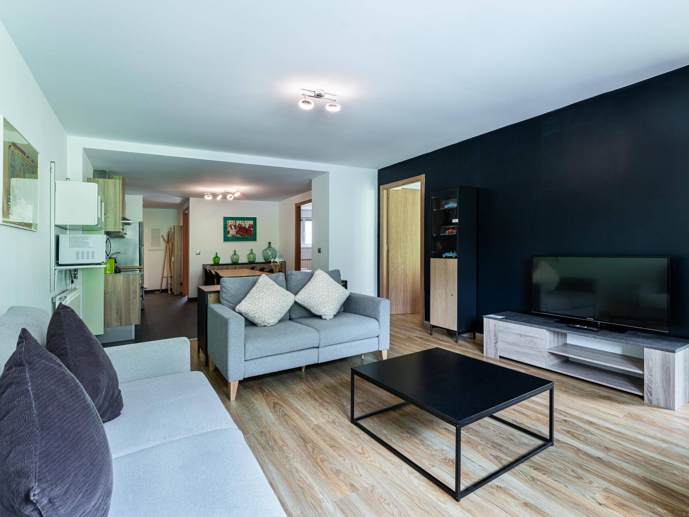 Een moderne woonkamer met een grijze bank, een zwarte salontafel en een flatscreen televisie.