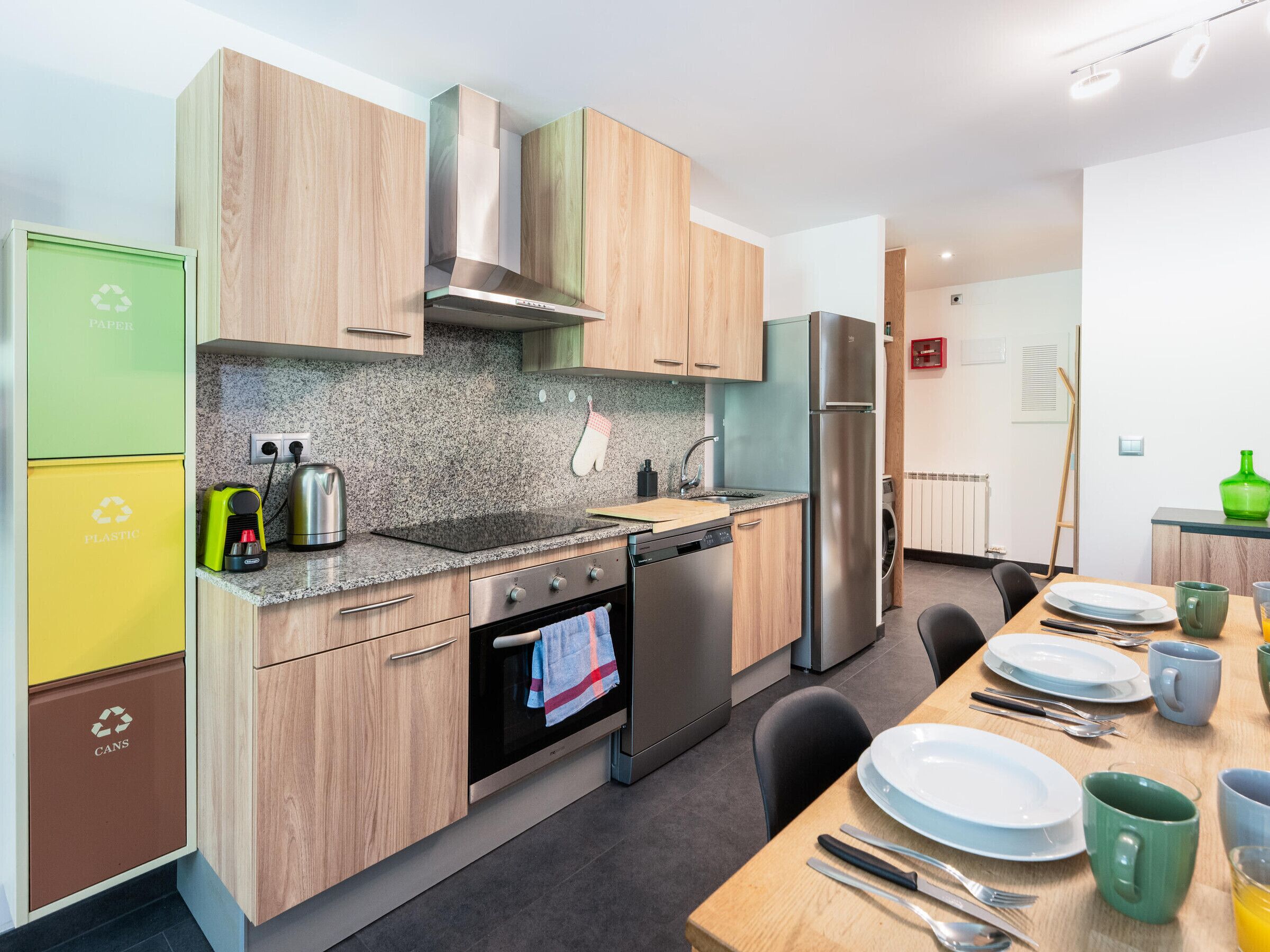 A modern kitchen with wooden cabinets, stainless steel appliances, and a dining area with a table set for two.