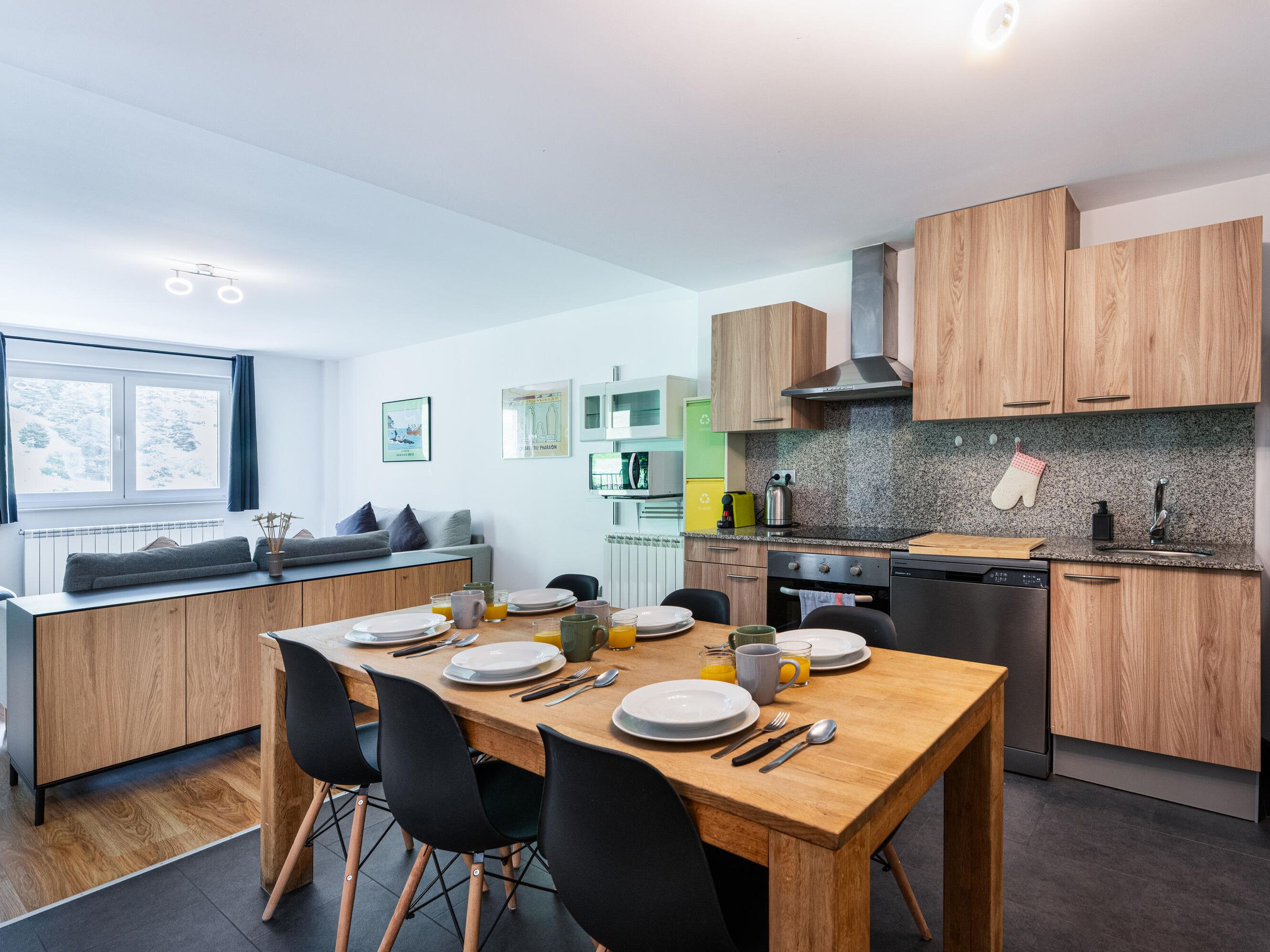Une cuisine moderne avec des meubles en bois, un plan de travail en granit et un coin repas comprenant une table en bois et des chaises noires.