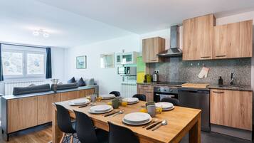 Une cuisine moderne avec des meubles en bois, un plan de travail en granit et un coin repas comprenant une table en bois et des chaises noires.