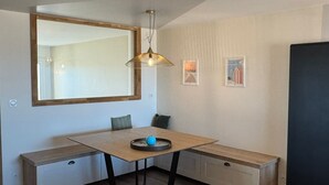 A modern dining area with a wooden table, bench seating, a hanging light fixture, and two framed pictures on the wall. - Charming apartment, sea view - 4 guests (Cabourg)