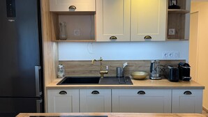 A modern kitchen with a built-in dishwasher, a sink with a faucet, and a coffee maker on the countertop. - Charming apartment, sea view - 4 guests (Cabourg)