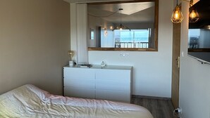 A hotel room with a bed, a dresser, a mirror, and a view of the outdoors. - Charming apartment, sea view - 4 guests (Cabourg)