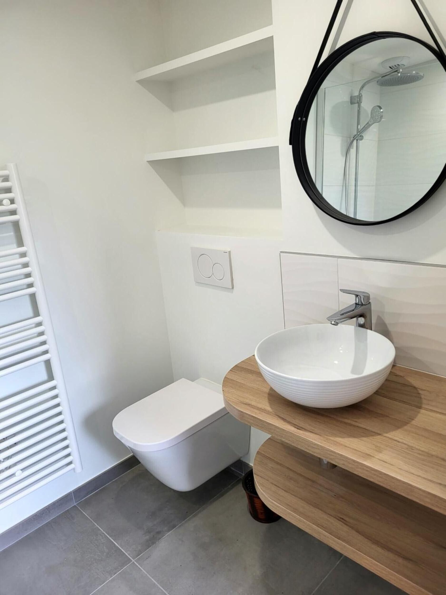 A modern bathroom with a white toilet, a white sink with a wooden countertop, a mirror, and a shower with a glass enclosure.