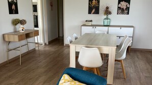 Ein moderner Essbereich mit einem Holztisch und weißen Stühlen, einer blauen Couch mit gemustertem Kissen sowie Kunstwerken an den Wänden.