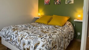 Ein Schlafzimmer mit floralem Bettbezug, zwei gelben Kissen und drei an der Wand hängenden Bildern.