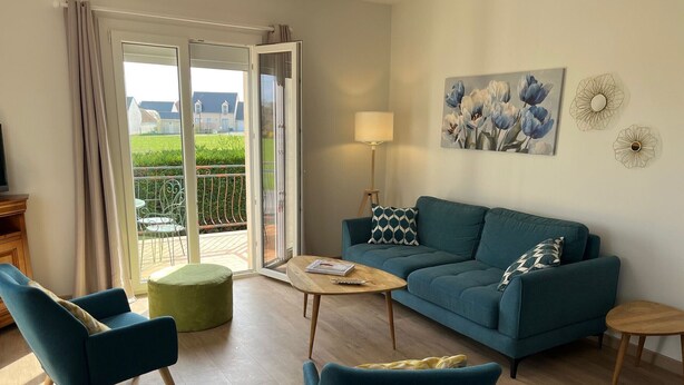 Ein Wohnzimmer mit einer Couch, zwei Sesseln, einem Couchtisch und einem Balkon mit Blick auf Häuser.