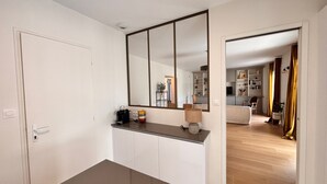 A room with a large mirror, a white door, a console table with a lamp, and a view into a living area with a sofa and a TV. - House with enclosed garden and veranda (LES SABLES D'OLONNE)