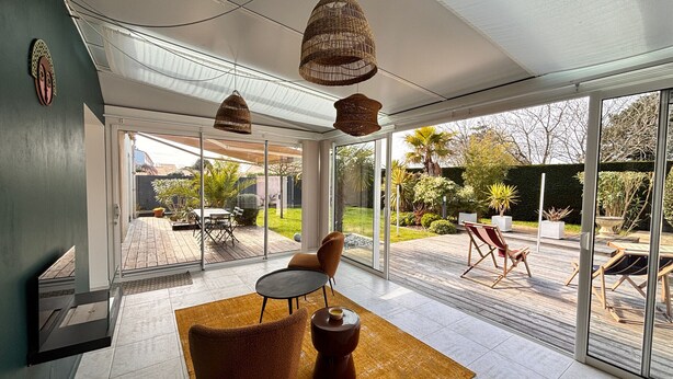 A modern interior with a glass door leading to a patio, a brown chair, a small table, and hanging wicker lamps. - House with enclosed garden and veranda (LES SABLES D'OLONNE)