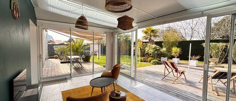A modern interior with a glass door leading to a patio, a brown chair, a small table, and hanging wicker lamps.