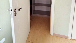 Una stanza con pavimento in legno, una porta bianca con maniglia e un armadio con ripiani multipli.