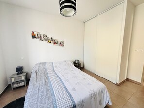 A bedroom with a bed, a nightstand, a lamp, a wardrobe, and a wall with photos. - Modern flat, private garden, 6 guests (Argelès-sur-Mer)
