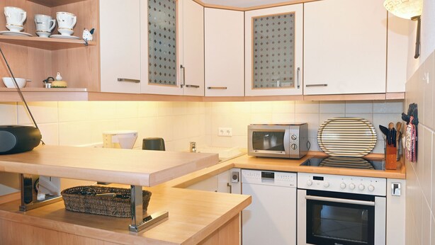 A kitchen with white cabinets, a microwave, an oven, and a wooden countertop. - Ostdeich Stübchen vacation apartment: Balcony & beach nearby (Büsum)